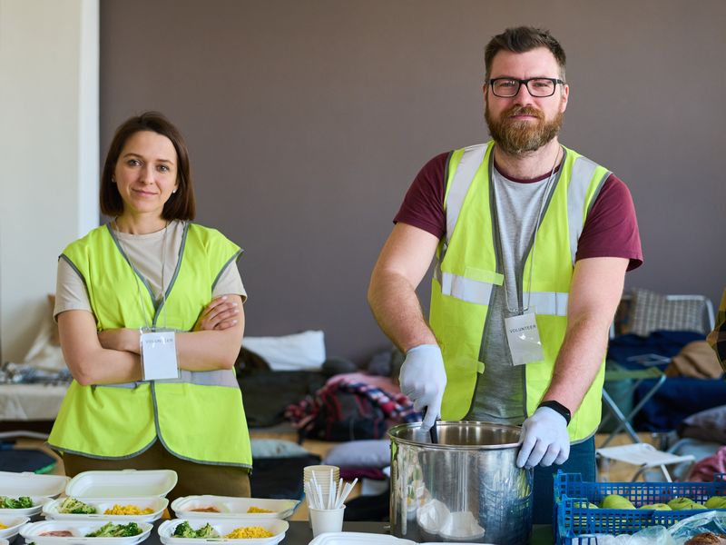 zwei ehrenamtliche Helfer helfen bei einer Essensausgabe