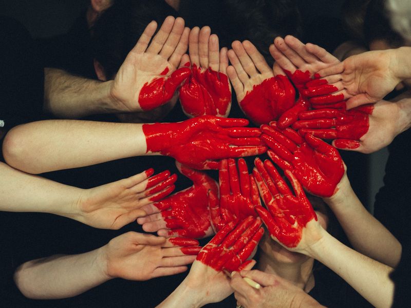 viele Menschen halten ihre bemalten Hände zu einer gemeinsamen Fläche zusammen, sodass ein Herz sichtbar wird